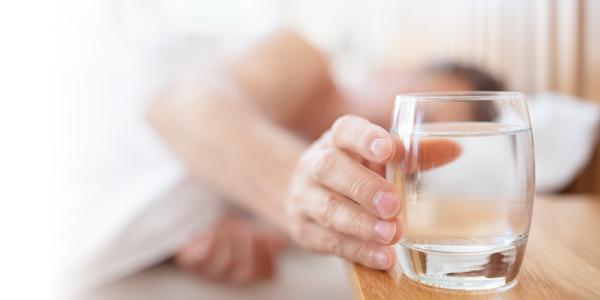 Closeup view of a hand extending to grab a glass of water on a bedside table Closeup view of a hand extending to grab a glass of water on a bedside table