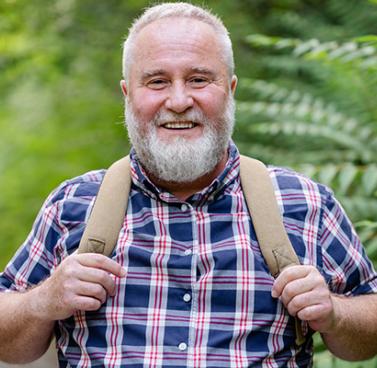 Elderly Man Enjoying a Forest Walk Wearing a Backpack and Smiling