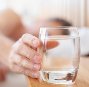 Closeup view of a hand extending to grab a glass of water on a bedside table